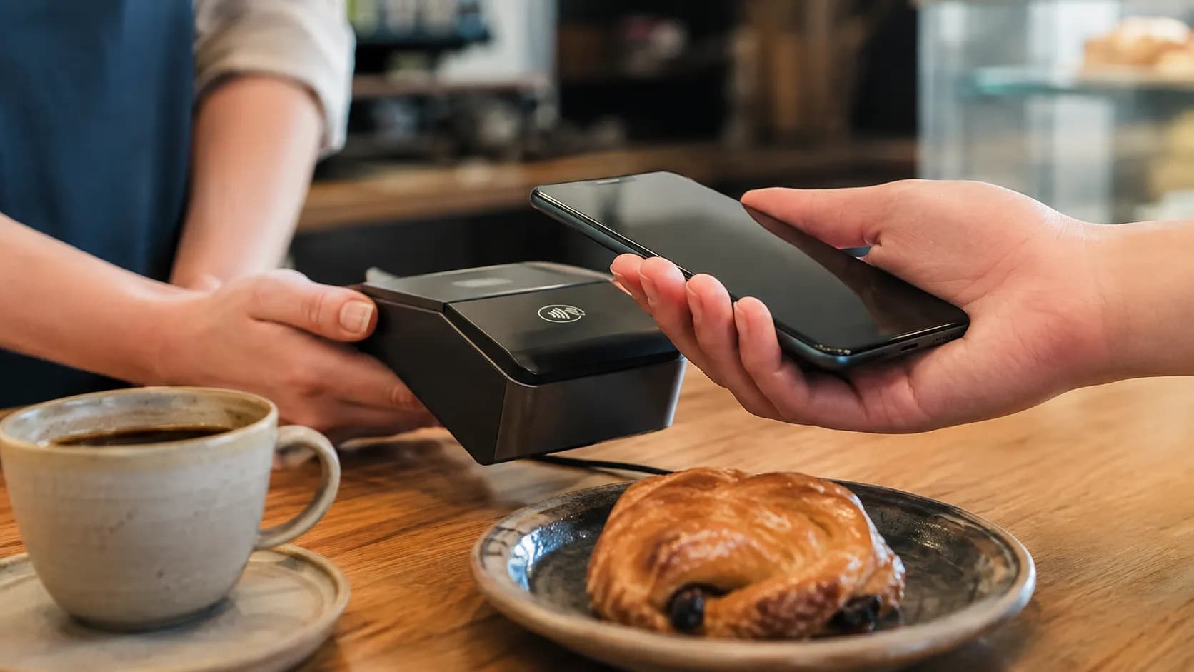 A hand using a phone for contactless payment at a café counter.