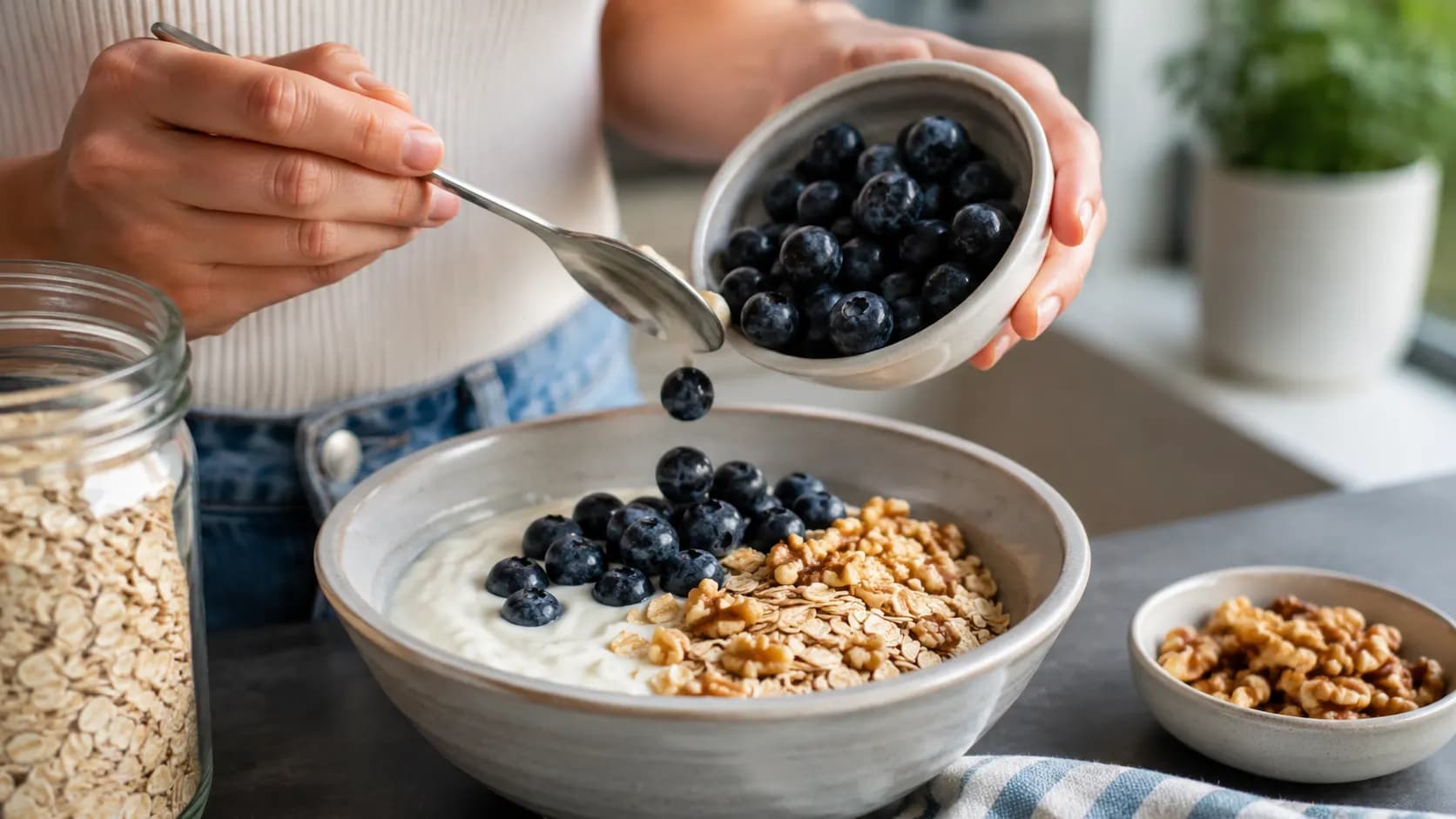 Blueberries being added to plain yogurt with oats and chopped walnuts.