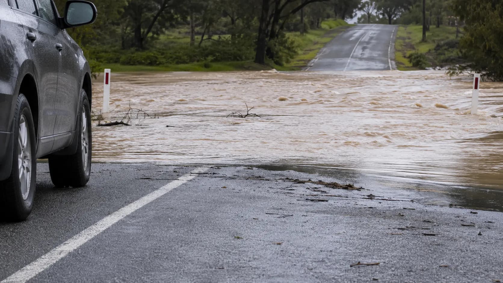 A vehicle stopped before a barrier where a road disappears beneath murky floodwater.