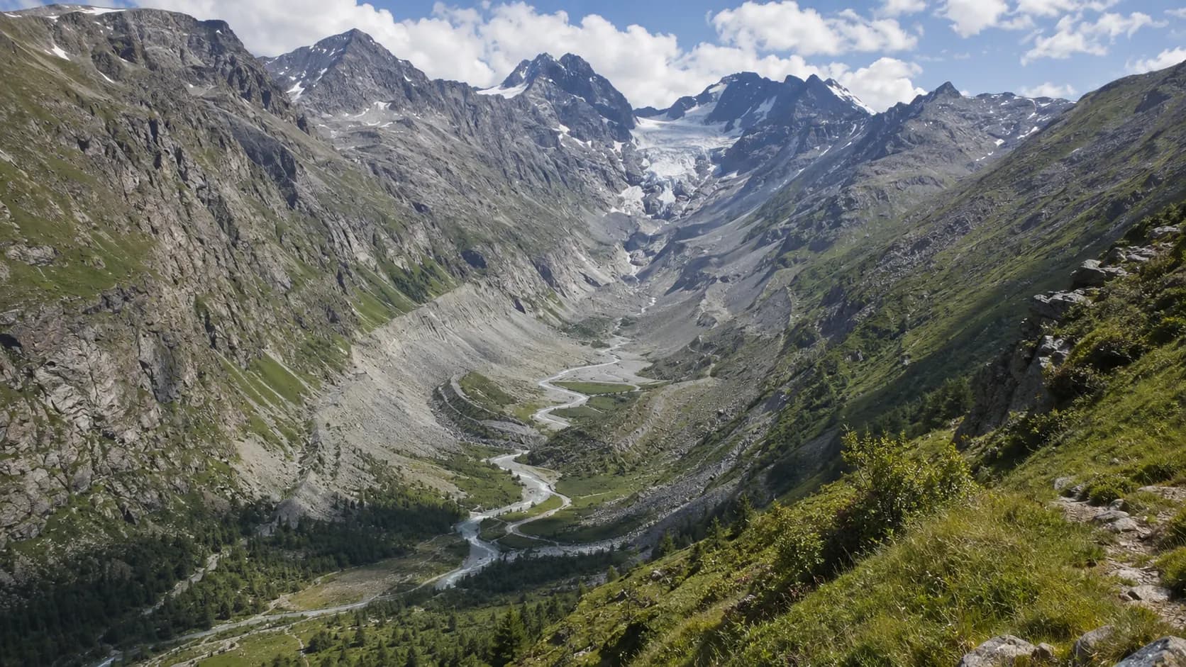 A U-shaped Alpine valley with steep sides, a river, moraine ridges and a glacier remaining high in the mountains.